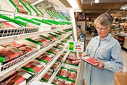 Photo: A woman looking at a package of meat in a grocery store. Link to photo information
